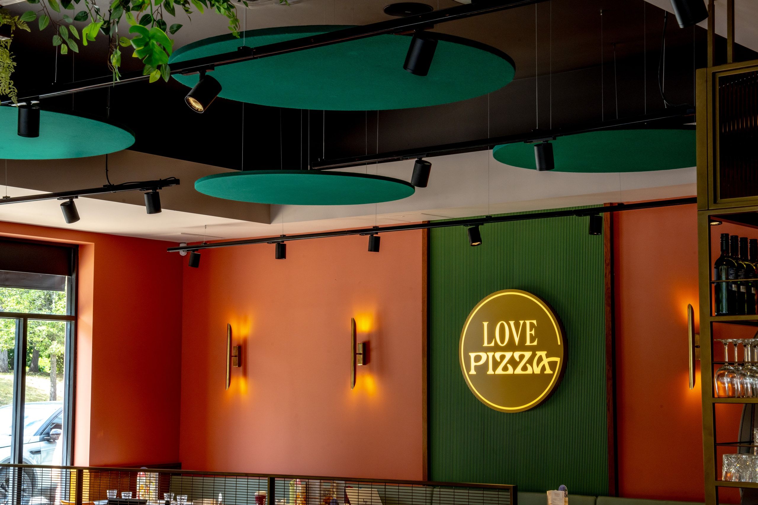 A decorated feature wall with illuminated Pizza Express signage and track lighting below green ceiling rafts.
