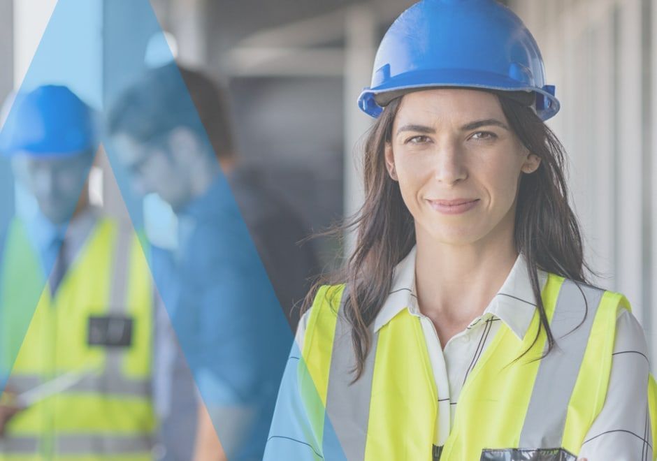 A woman in a hard hat and hi-vis vest on a construction site, with colleagues behind her.